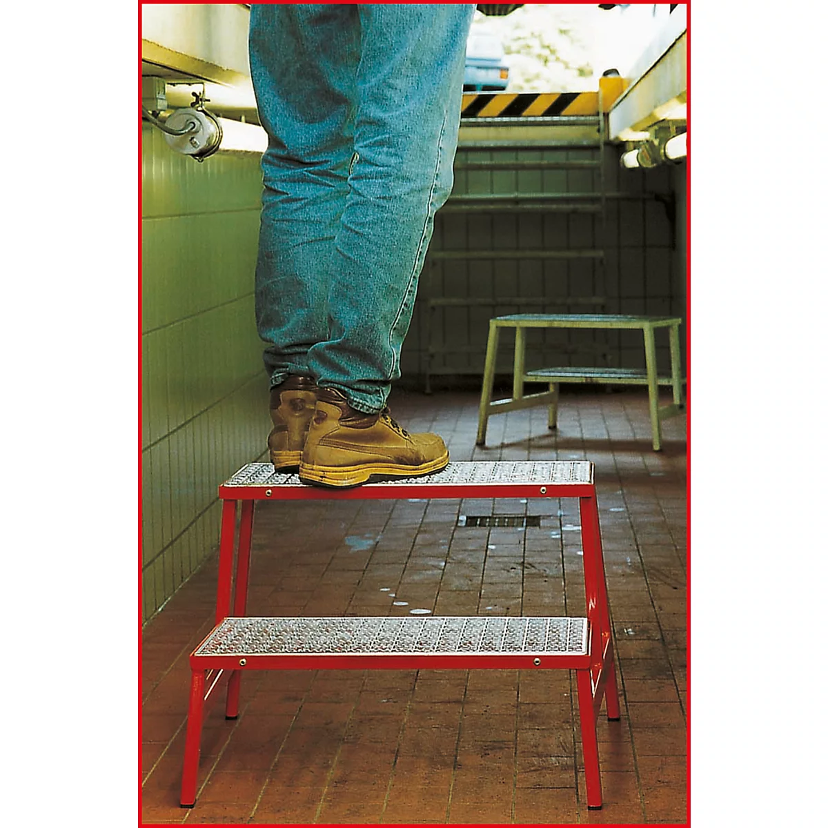 Person steht auf roter Trittleiter in Waschraum. Braune Stiefel, Jeans, Fliesen. Auf dem Boden, steht eine weitere Trittleiter.